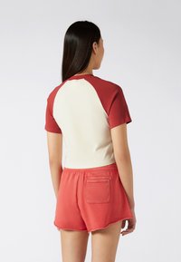 Red and cream short-sleeve shirt with a raglan design and smooth texture, paired with red shorts featuring a pocket and frayed hem.