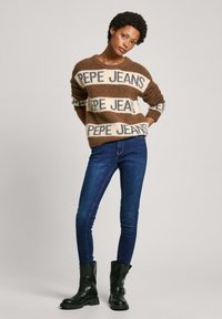 Maglione a righe marroni e crema con logo "PEPE JEANS", realizzato in materiale morbido. Abbinato a jeans skinny blu scuro e stivali neri alla caviglia.