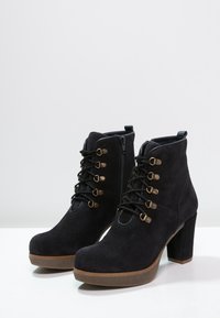 Czarne zamszowe botki za kostkę na masywnej obcasie, z przodem na sznurówki, zamkiem błyskawicznym i mosiężnymi detalami. Teksturowane gumowe podeszwy zapewniają przyczepność.