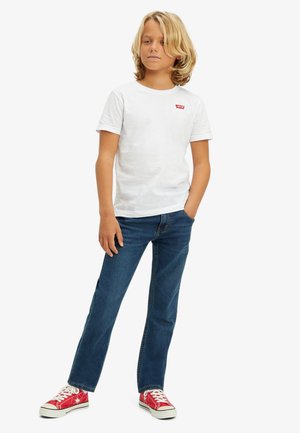 T-shirt en coton blanc avec un logo rouge, associé à un jean bleu et des baskets rouges. Le jean a une coupe classique et des détails de couture subtils.