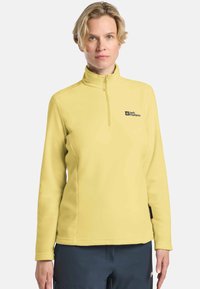 Gelbes Fleece-Pullover mit hohem Kragen, Reißverschluss vorne und gesticktem Logo. Glatte Textur, lange Ärmel und lockere Passform.