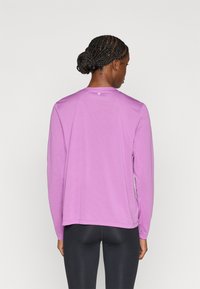 Αθλητική μπλούζα με μακριά μανίκια σε ανοιχτό μωβ χρώμα, κατασκευασμένη από αναπνεύσιμο ύφασμα, με στρογγυλή λαιμόκοψη και διακριτικό υφασμάτινο μοτίβο στην πλάτη.