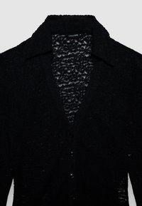 Schwarze Spitzenstrickjacke mit V-Ausschnitt, Knopfleiste und strukturiertem Muster. Verfügt über einen breiten Kragen und transparente Details durchgehend.