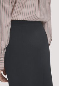 Schwarzer, gerippter Bleistiftrock mit einem glatten Bund, kombiniert mit einem hellrosa gestreiften Hemd mit Knopfmanschetten, das Details aus der Seitenansicht zeigt.