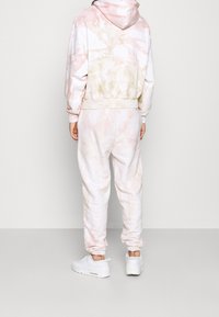Felpa e pantaloni tie-dye in colori pastello rosa e crema, realizzati in materiale morbido, con polsini elastici e cappuccio.
