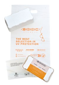 Estuche de gafas blancas con bordes redondeados, una superficie texturizada y una etiqueta naranja en contraste, junto a una bolsa compostable blanca con detalles impresos.