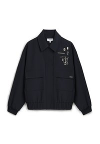 Veste noire courte en tissu lisse, avec deux poches avant, une fermeture à boutons et des accents décoratifs en métal argenté.