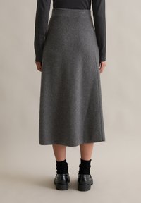 Fustă midi din lână gri, cu talie ajustată, siluetă A-line și margini curate, asortată cu șosete negre și pantofi negri masivi.