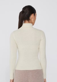 Helles Creme, geripptes Rollkragensweater mit langen Ärmeln. Verfügt über eine figurbetonte Silhouette und eine weiche Textur und zeigt ein nahtloses Design.