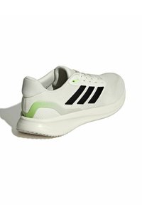 Zapatilla blanca con parte superior texturizada, logotipo de tres franjas negras, acento verde en el talón y una suela ligera diseñada para la comodidad.