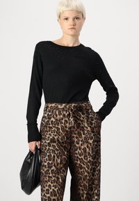 Čierny sveter s dlhým rukávom a zdobením z korálok, kombinovaný s voľnými nohavicami s leopardím potlačou. Modelka drží čiernu kabelku.