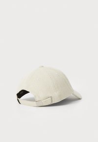 Corduroy baseball cap in light beige with a curved brim, featuring white eyelets and an adjustable strap back with a metal buckle.