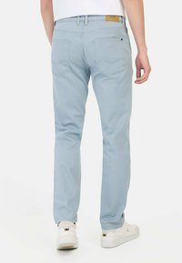 Jasnoniebieskie dżinsy o prostym kroju, pięć kieszeni, brązowa metka na pasku; gładka faktura i minimalne detale.
