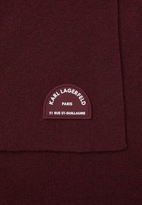 Burgundi kötött anyag sima felülettel és egy lekerekített címkével, amelyen a "KARL LAGERFELD PARIS" felirat és a "21 RUE ST-GUILLAUME" cím található.