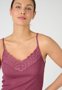 Maroon tank top with adjustable spaghetti straps, featuring a lace trim along the V-neckline. Smooth texture and fitted design.