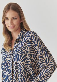 Satiinist blouse, millel on tumesinine abstraktne lehemuster beežil taustal, klappkrae ja lõdvad varrukad.