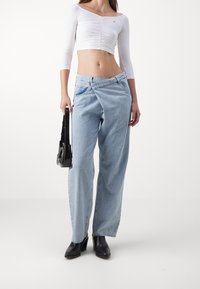 Vaqueros de pierna ancha en azul claro con una textura ligeramente arrugada, combinados con un crop top blanco ajustado y botas de tacón alto negras. Bolso negro.