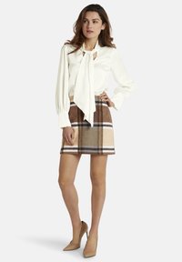 Balta satīna blūze ar saiti apkakles daļā, kopā ar brūnu svītrainu mini svārku. Tērps ietver augstpapēžu kurpes un garas piedurknes.