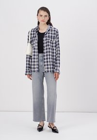 Modra in bela karirana oversize srajca, prilegajoča črna majica, visoki sivi jeans in črne čevlje z ostrim nosom. Enostavna torbica.