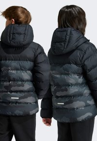 Veste rembourrée en camouflage noir et gris, dotée d'une capuche amovible, de panneaux matelassés et de détails réfléchissants dans le dos.