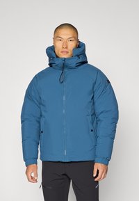 Blå isolerad jacka med dragkedja, justerbar huva och elastiska ärmar. Strukturerad tyg och sidofickor med tryckknappar.