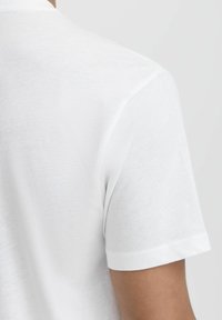 Fehér pamut póló, kerek nyakkal, rövid ujjú, sima textúrával, látható varrási részletekkel és enyhe fénylő felülettel.