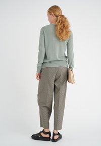 Maglione verde chiaro, pantaloni grigi a fantasia e sandali neri. Il maglione presenta un collo rotondo e polsini a coste. Borsa a mano.