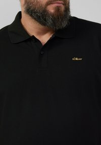 Zwart poloshirt met een klassieke kraag, voorzien van drie knopen. Het heeft een gestructureerde stof en een klein gouden s.Oliver-logo op de borst.