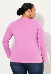 Dlouhý rukáv T-shirt z vibraní růžové tkaniny. Přiléhavý střih s kulatým výstřihem, hladká textura a šití na okrajích. Nosit s tmavými džíny.