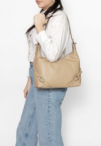 Beige leren handtas met een slouchy ontwerp, zilveren hardware accenten en decoratieve stiksels aan de zijkanten. Enkele schouderband.