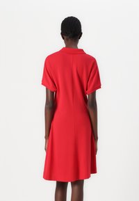 Robe rouge à manches courtes avec col, offrant une coupe décontractée et un ourlet évasé, fabriquée en tissu lisse, vue de dos.