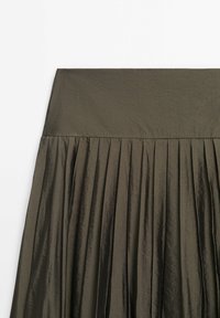 Section de jupe plissée vert olive foncé avec large ceinture et tissu subtilement texturé sur fond blanc.