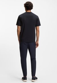 Czarny bawełniany t-shirt z krótkimi rękawami, zestawiony z granatowymi dresami z elastycznymi mankietami i dopasowanym krojem, pokazany od tyłu.