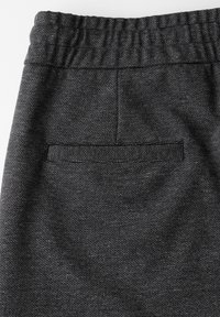 Černé textured běžecké kalhoty s elastickým pasem, které mají zadní kapsu zvýrazněnou tkaným pruhem podél horní části.