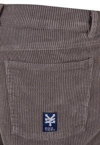 Grijze corduroy stof met verticale ribbels, een achterzak en een marineblauwe label met het "ZOO YORK" logo erop gestikt.