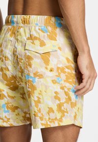 Maillots de bain avec taille élastique, motif abstrait jaune et bleu, texture douce, poche arrière avec rabat et détail sur la couture latérale.