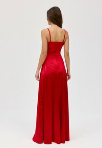Dlouhá červená saténová šaty s tenkými ramínky, přiléhavým korzetem a splývavou sukní. Na zádech je diskrétní zip.