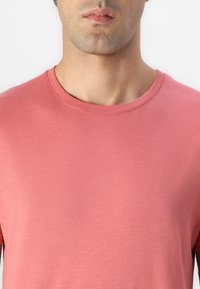 T-shirt s kratkim rukavima i okruglim izrezom izrađen od meke, teksturirane pamučne tkanine, u solidnoj prigušenoj ružičastoj boji. Jednostavan dizajn bez uzoraka.