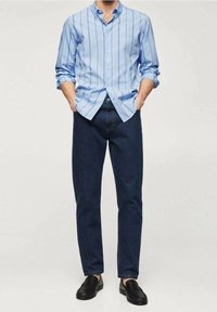 Camisa de botones azul claro con rayas verticales, combinada con jeans de mezclilla azul oscuro y mocasines negros. Textura lisa, corte clásico.