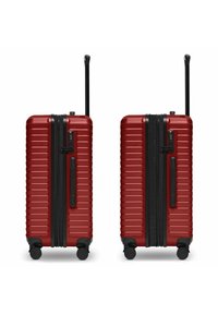 Maleta dura roja con textura estriada, cremallera negra, asas dobles y cuatro ruedas. Incluye un candado aprobado por la TSA y un asa retráctil.