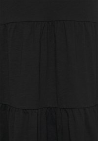 Svart tyg med en mjuk textur har en lagerdesign, bestående av samlade volanger som skapar en svävande silhuett.