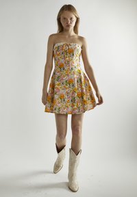 Vestido floral sin mangas en tonos pastel con flores anaranjadas y rosas, falda acampanada y un detalle de encaje alrededor del escote, combinado con botas de cowboy blancas.