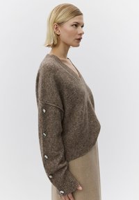 Pulover maro tricotat cu decolteu în V, tiv cu dungi și nasturi mari argintii pe mâneci. Textură moale cu croială largă, supradimensionată.