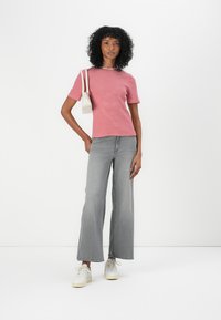 Tricou cu maneci scurte, cu dungi roșii și albe, asortat cu blugi evazați gri și adidași crem; modelul ține o geantă mică albă.