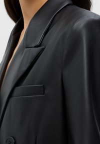 Czarna skórzana marynarka o błyszczącym wykończeniu, z szerokim klapą, jedną kieszenią i dwiema guzikami. Gładka faktura z dopasowanym krojem.