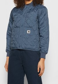 Granatowa pikowana kurtka z zapięciem na zatrzaski, ściągaczami u dołu rękawów oraz naszywką z logo na piersi. Wykonana z gładkiego, lekkiego materiału.