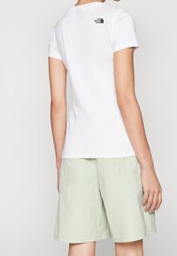 Vit bomull t-shirt med korta ärmar, som har en liten svart logga på baksidan. T-shirten är matchad med ljusgröna knälånga shorts.