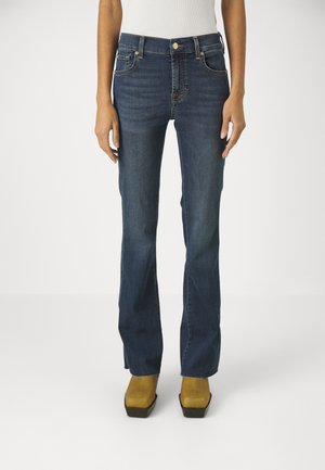 Pantalones vaqueros de mezclilla azul oscuro con un diseño de pierna recta, equipados con bolsillos y herrajes metálicos, combinados con zapatos de plataforma amarillos.
