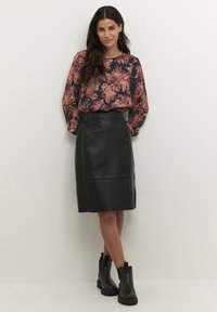 Blusa a maniche lunghe con motivo floreale nero, abbinata a una gonna a matita in pelle nera e stivaletti neri con suola spessa.