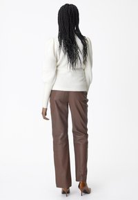 Cream sweater with puff sleeves, paired with brown leather trousers. The outfit is completed with brown pointed heels.
